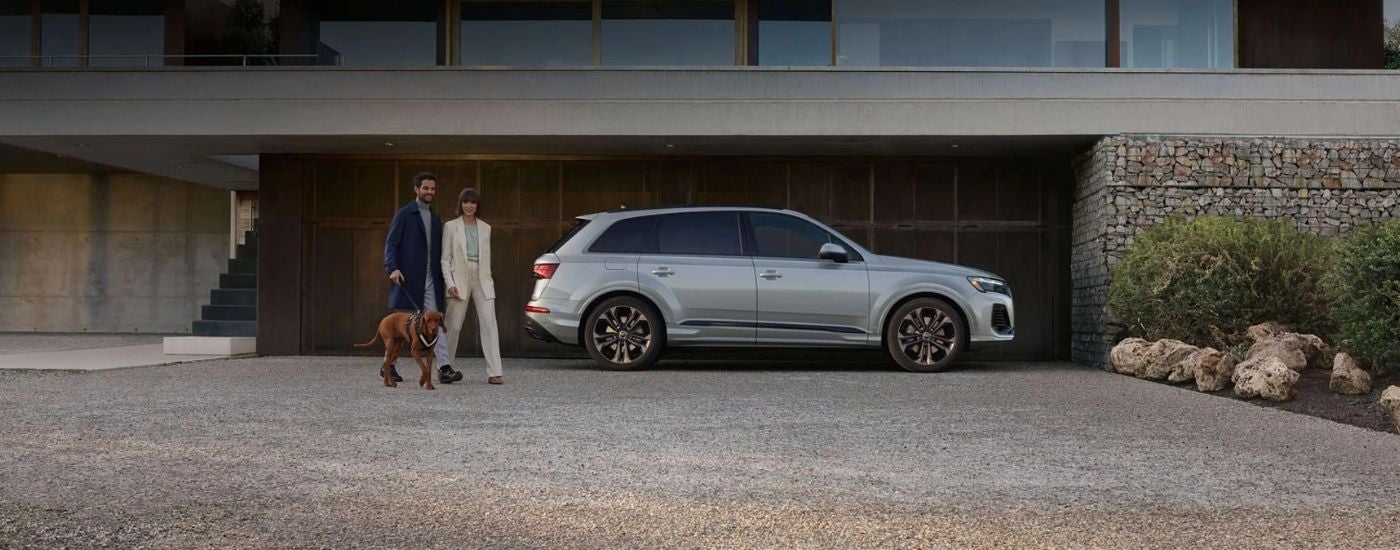 Couple and a dog walking next to a silver 2025 Audi Q7.